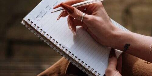 Woman with long manicure taking notes in copybook