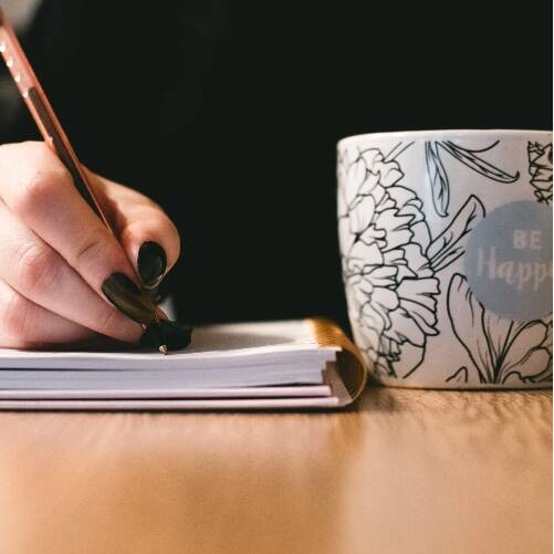 Person holding pen and writing, coffe mug on the side